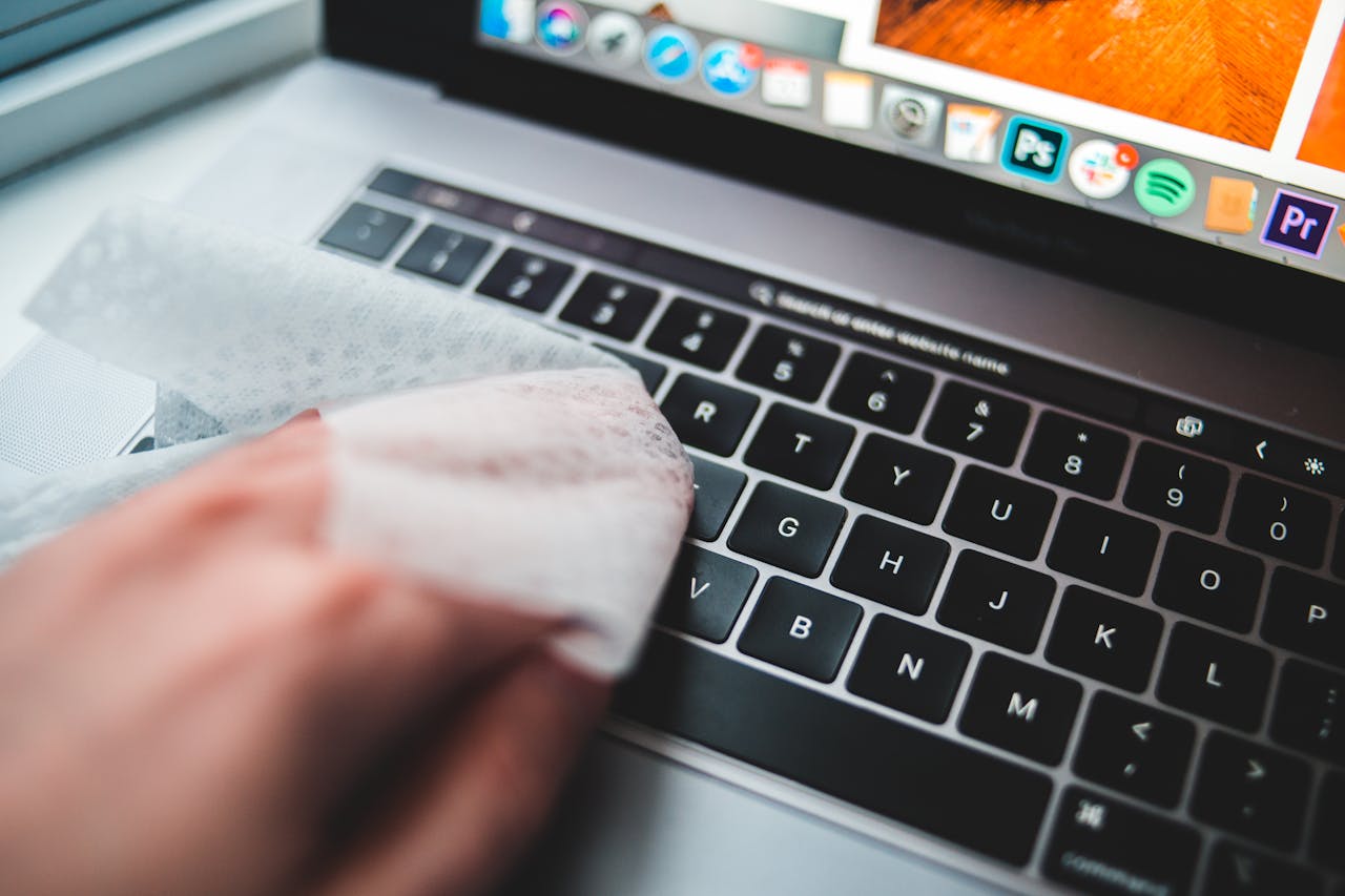 heros-img Person cleaning a laptop keyboard using disinfectant wipes for hygiene.